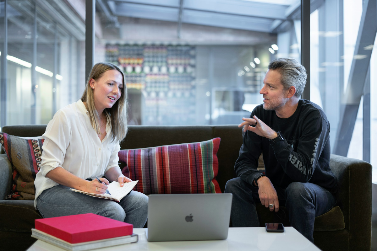Zwei Personen auf einer Couch im Büro vor einem Laptop